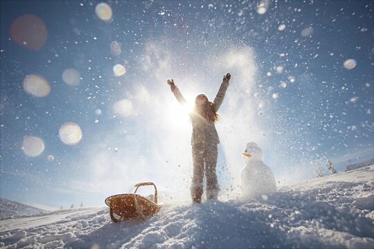 Child playing in the snow near a snowman on a sunny winter day