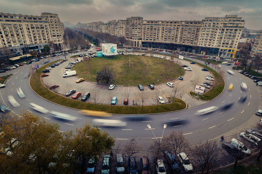 Aerial view of a large circular roundabout with heavy traffic and motion blur, surrounded by dense urban apartment blocks in Bucharest, Bucharest, Romania.