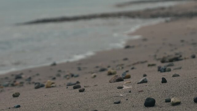Low angle view of numerous small stones washed ashore on a beige sandy beach
