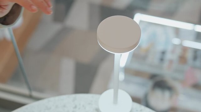 Close up of woman hand interacting with and turning on elegant white circular table lamp illuminating its soft glow. interaction highlights smooth texture and modern design as it lights