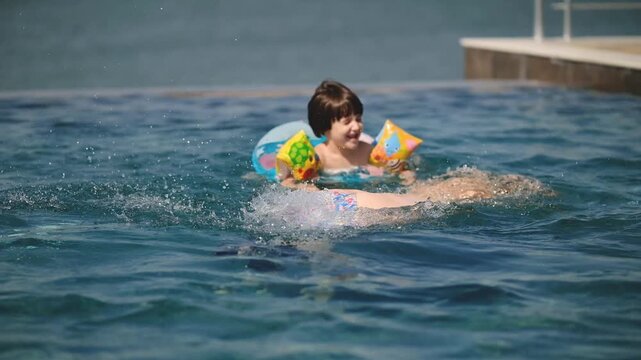 Happy Little Boy Swimming with Inflatable Ring in Pool as Mother Dives Under Water