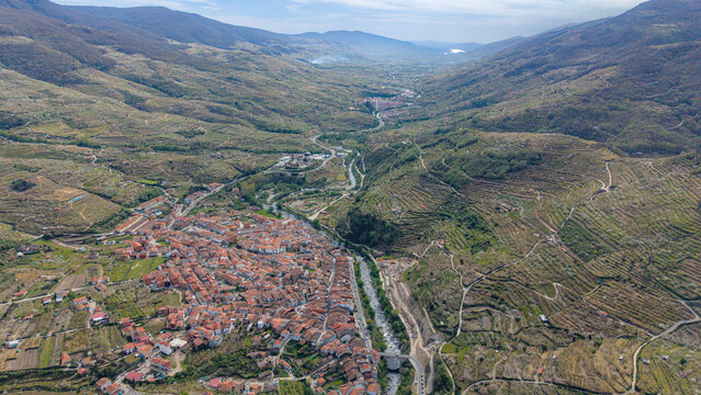 Aerial view of Cabezuela del Valle with traditional terracotta-roofed houses, terraced hillsides, and the Jerte River flowing through the landscape in Cabezuela del Valle, Extremadura, Spain.