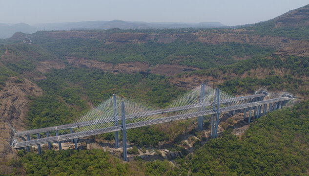 Aerial view of the Missing Link Suspension Bridge spanning a lush green valley with highway tunnels and mountainous terrain in Lonavala, Maharashtra, India.
