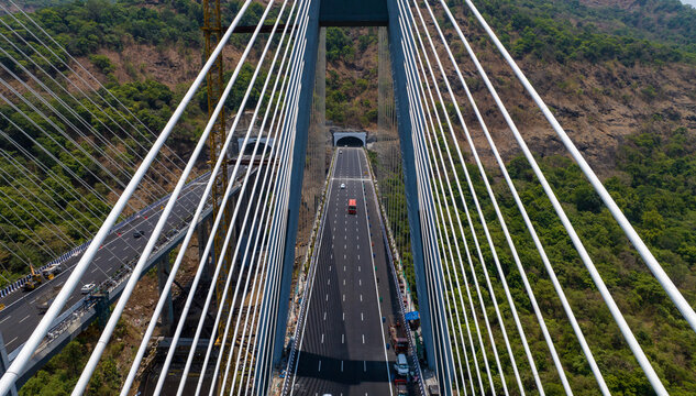 Aerial view of the Missing Link Suspension Bridge with vehicles traveling on the highway through tunnels surrounded by lush green hills in Lonavala, Maharashtra, India.