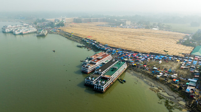 Aerial view of Charmonai riverbank with passenger ferries docked near a bustling market and mosque in Charmonai, Barisal Division, Bangladesh.
