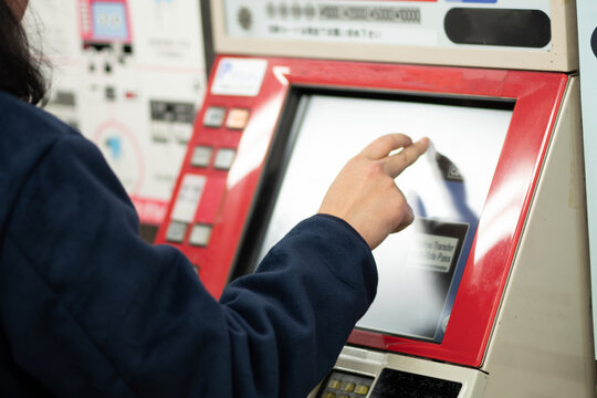 Close-up of a person's hand touching the screen of an automated ticket vending machine at a subway station in Osaka, Japan.