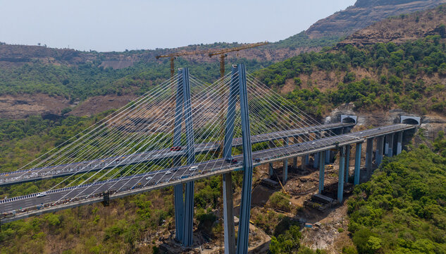 Aerial view of the Missing Link Suspension Bridge on the Mumbai-Pune Expressway surrounded by lush green hills and tunnels in Lonavala, Maharashtra, India.