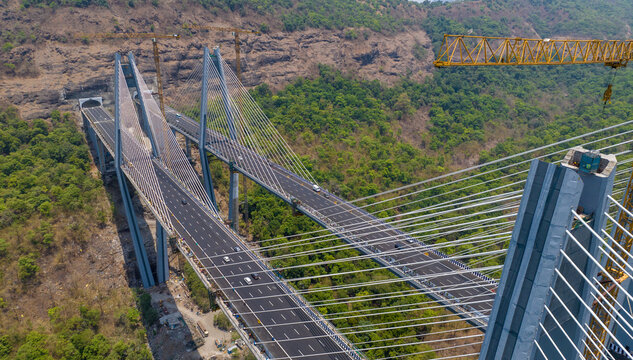Aerial view of the Missing Link cable-stayed bridge on the Mumbai-Pune Expressway, featuring construction cranes and lush green hills in Lonavala, Maharashtra, India.