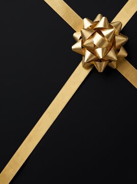 A gold ribbon bow crosses over itself, isolated on a plain black background, ready for gift wrapping design.