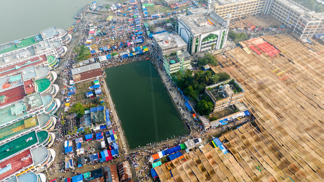 Aerial view of the Charmonai mosque and gathering area with temporary tents, a central pond, and boats docked along the riverbank in Charmonai, Barisal Division, Bangladesh.