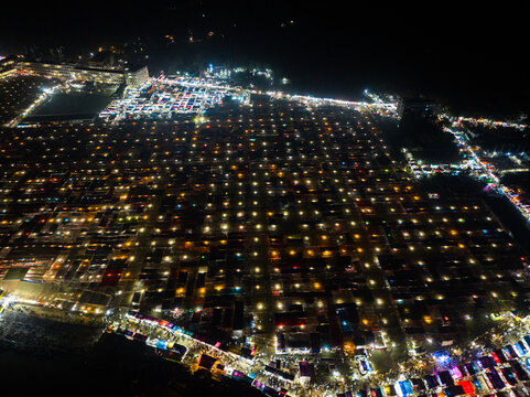 Aerial view of the illuminated Charmonai Mahfil gathering at night with rows of tents and bright lights stretching across the landscape in Charmonai, Barisal Division, Bangladesh.