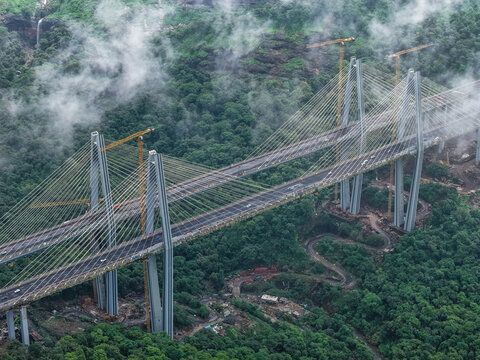 Aerial view of the Missing Link Suspension Bridge spanning across a lush green forested valley with construction cranes and misty clouds in Lonavala, Maharashtra, India.
