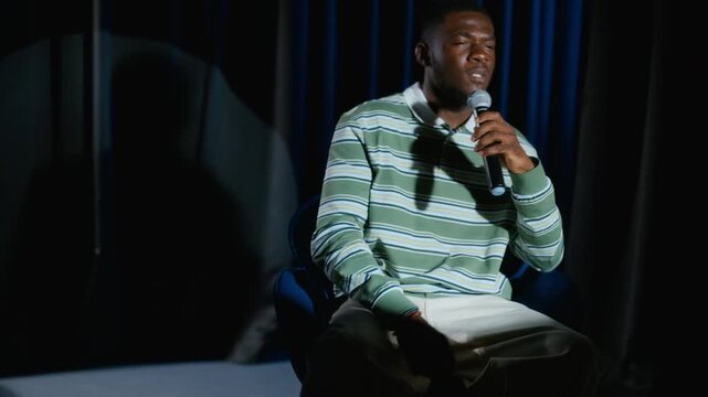 African American young man sitting on stage holding microphone and delivering emotional monologue in slow motion. Clip ideal for drama school and acting workshop promos