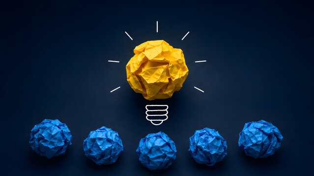 Yellow crumpled paper lightbulb hovering above blue paper balls representing unique business idea standing out from the crowd and leadership