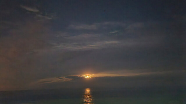 Moonlight filtering through stratocumulus beneath an altostratus veil, creating a layered atmospheric scene over the calm Mediterranean Sea at night