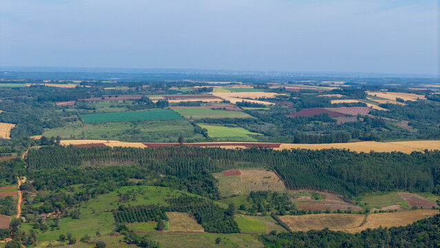 Aerial view of agricultural fields, patches of forest, and rolling hills under a clear sky in Nueva Alborada, Itapua Department, Paraguay.