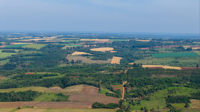 Aerial view of the rolling agricultural landscape featuring a patchwork of green fields, golden crops, and patches of forest in Nueva Alborada, Itapua Department, Paraguay.