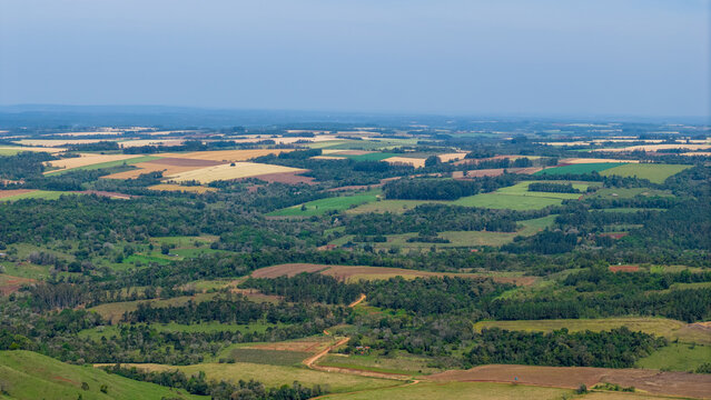 Aerial view of the rolling agricultural landscape with patchwork fields, dense forests, and winding dirt roads in Nueva Alborada, Itapua Department, Paraguay.