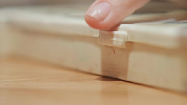 Close up of hand opening latch on old plastic container revealing its contents. action is captured in soft lighting with shallow depth of field focusing solely on interaction between finger