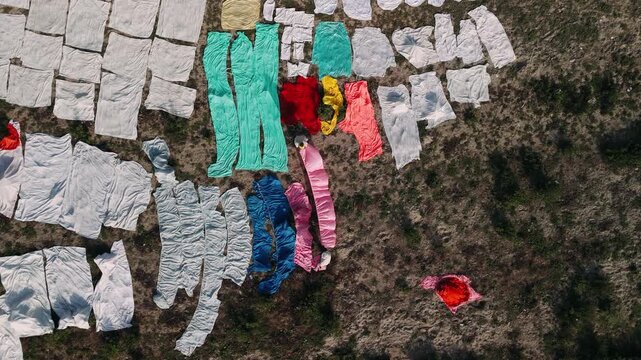 Aerial view of a dhobi worker drying colorful laundry to dry in the sun on the ground in india, showing traditional practices