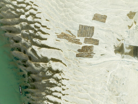Aerial view of sandy riverbanks with patterns of drying crops on the silt and a small boat along the water in Rajshahi, Rajshahi Division, Bangladesh.