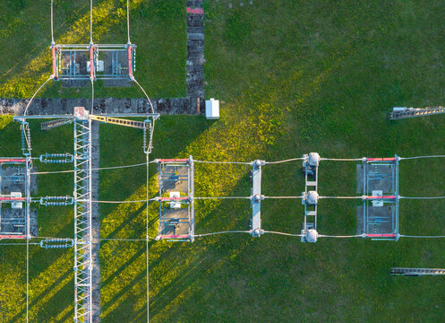 Aerial view of an electrical substation with power lines, transformers, and metal structures set against a grassy field during the golden hour in Gdynia, Pomeranian Voivodeshi, Poland.