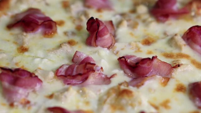 Closeup of baked pizza with melted cheese, ham and bacon pieces on top. Italian food texture detail. Delicious fast food meal for pizzeria menu and restaurant concept.