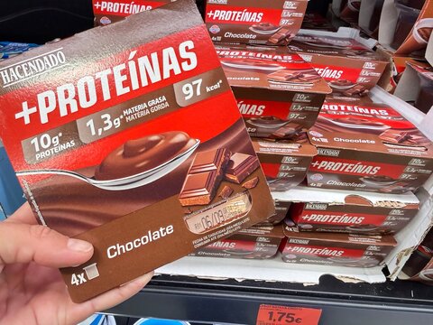 Mallorca, spain, august 30, 2026, hand holding hacendado plus proteinas chocolate pudding in a supermarket aisle, emphasizing healthy eating and protein