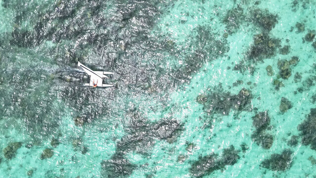 Aerial view of a small catamaran sailing across clear turquoise lagoon waters with visible coral reefs in Trou-aux-Biches, Pamplemousses District, Mauritius.