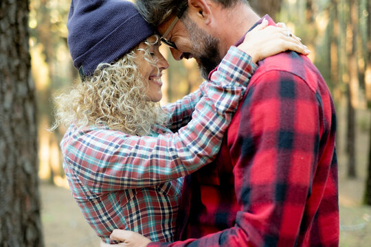 Couple expressing strong connection and happiness, embracing outdoors in a forest, enjoying a romantic moment together while dressed in comfortable plaid shirts and hats