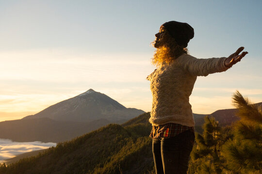 Woman standing with arms open on a mountain viewpoint, enjoying breathtaking panoramic views of mount teide volcano and a stunning sunset over the natural landscape, feeling freedom and happiness