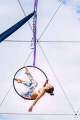 Acrobat woman on an aerial hoop performs a graceful, athletic trick against a bright sky, showcasing flexibility, strength, balance and circus artistry during an outdoor performance © simona