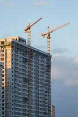 Fototapeta premium Yellow tower cranes constructing modern high rise residential building at sunset