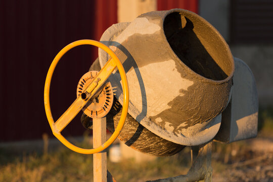 Portable concrete mixer with yellow handwheel standing on a construction site at sunset