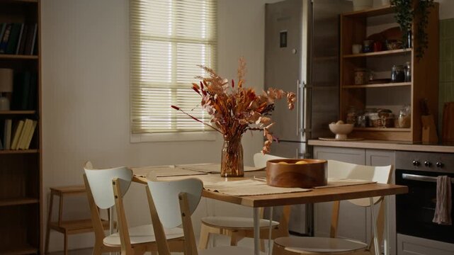 Dining table with dried floral vase and wooden fruit bowl standing in modern residential kitchen. Footage fitting for real estate promos, interior design ads and family lifestyle campaigns