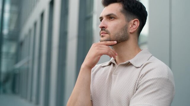 Close up pensive young Caucasian business man thinking holding chin looking at camera serious expression in city. Portrait thoughtful businessman male guy worker think work strategy posing outside