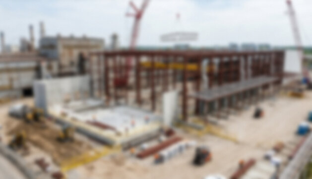 A large construction site featuring a steel framework of a building under construction, with cranes and machinery visible, reflecting industrial progress.