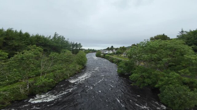 FPV drone flight over a typical Scottish river, or burn. Shot in Poolewe in the Highlands of Scotland the flight follows the course of the river through a typical village setting.