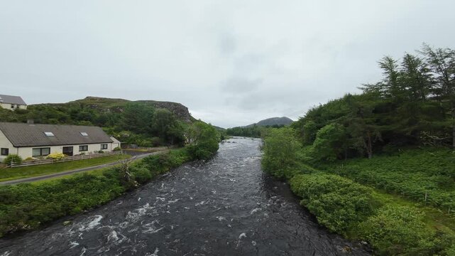 FPV flight over a Scottish river, or burn. Shot in Poolewe in the Highlands of Scotland the flight follows the course of the river through a typical village setting. The local church is visible.