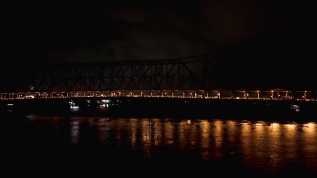 Lateral drone shot moving right to left past illuminated Howrah Bridge, with night traffic and golden reflections on the Hooghly River.
