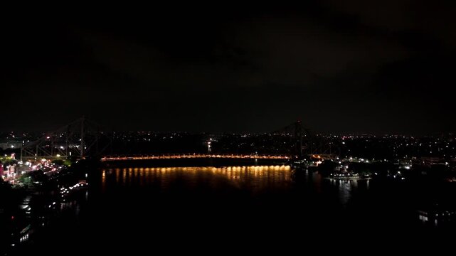 Aerial drone push in toward illuminated Howrah Bridge at night, with traffic crossing the bridge and reflections on the Hooghly River.