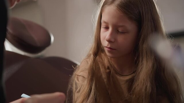 Close up of young girl sitting in orthodontic clinic while another girl likely dentist works on her teeth. scene shows dental tools and materials being used for treatment indoors with soft
