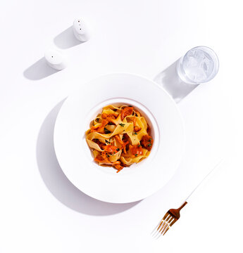 Classic pasta with chanterelles, fork and water glass on white background. Italian food dish rich in wild mushrooms and carbohydrates. Authentic vegetarian meal, top view healthy eating.