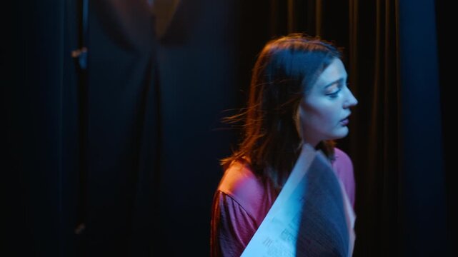 Caucasian young woman rehearsing script backstage and fanning herself with paper during theater audition. Useful for performing arts education, casting call promotions, and stage fright concepts