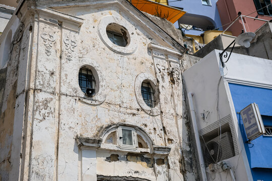 Procida, Italy - August 7, 2026. Weathered Architectural Detail of an Ancient Chapel Facade in Procida. A detailed, low-angle shot showcasing the weathered and peeling plaster facade of an ancient cha