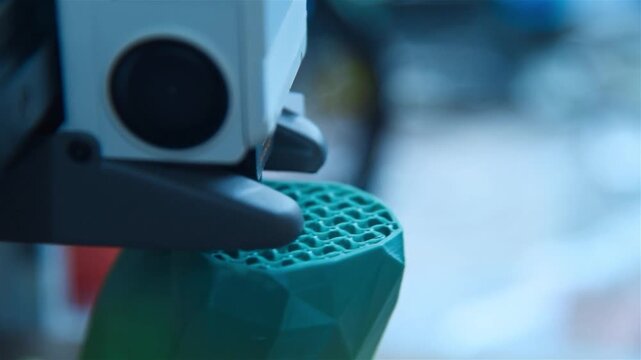 3D printer nozzle creating a green plastic object.