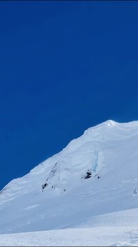 Aerial footage of a skier navigating a steep snowy mountain slope under bright blue sky conditions skiing winter sports alpine landscape