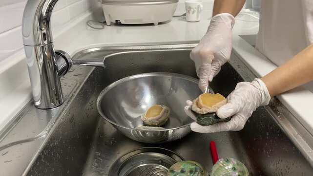 Separating abalone meat from its shell using a spoon in a kitchen sink