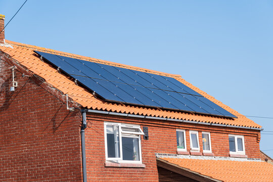 Standard on-roof solar panels mounted on rails on a modern red brick detached house rooftop in the UK