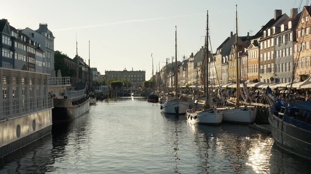 Historic sailboats and wooden vessels moor along the famous Nyhavn canal in Copenhagen. Colorful townhouses line the lively waterfront promenade. Danish culture and European vacation concept.